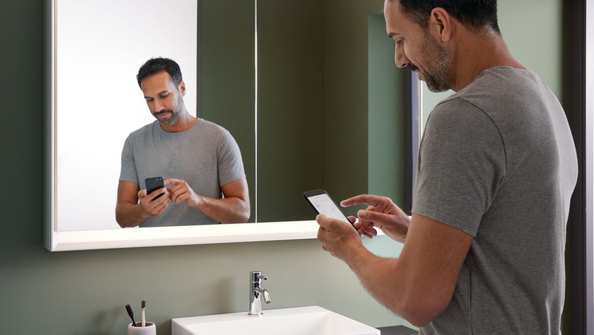 Man staat in de badkamer met een mobiele telefoon