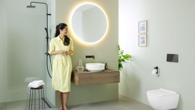 Vrouw in gele jurk voor mintgroene badkamer met meubels en badkamerkeramiek van Geberit en zwarte kranen