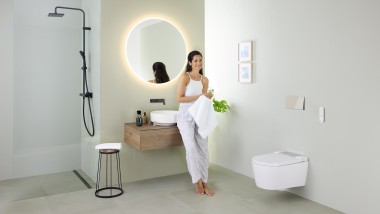 Vrouw leunt op een wastafel in een badkamer met Geberit AquaClean Sela toiletsysteem en Geberit VariForm-wastafel en meubel