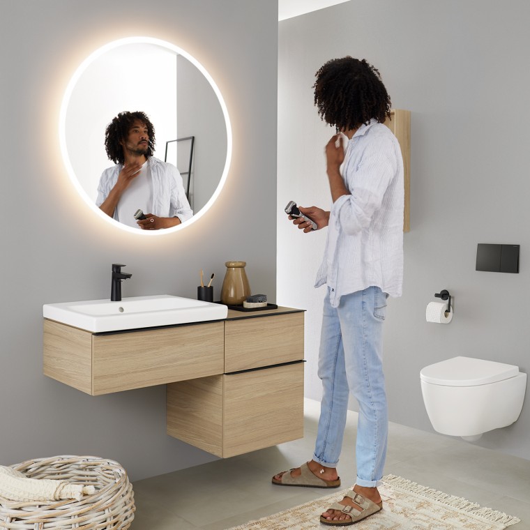 Man bekijkt zichzelf in een ronde verlichte Geberit Option spiegel Man bekijkt zichzelf in een ronde verlichte Geberit Option spiegel