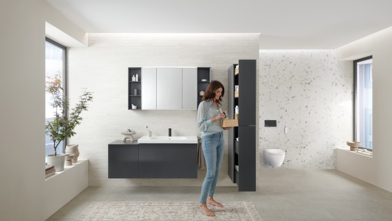 Femme ouvrant une colonne haute avec beaucoup d‘espace de rangement dans une salle de bains avec meubles de salle de bains Geberit Acanto Femme ouvrant une colonne haute avec beaucoup d‘espace de rangement dans une salle de bains avec meubles de salle de bains Geberit Acanto