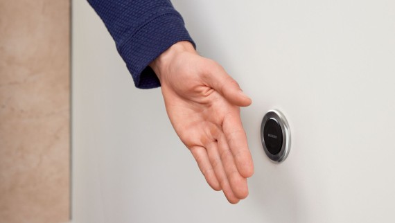 Une main actionne la commande à distance ronde sans contact Geberit type 10 Une main actionne la commande à distance ronde sans contact Geberit type 10