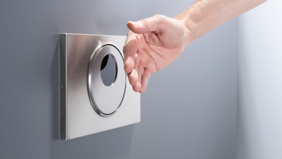 Une main actionne la commande à distance de la plaque de commande sans contact ronde Geberit Sigma10 Une main actionne la commande à distance de la plaque de commande sans contact ronde Geberit Sigma10