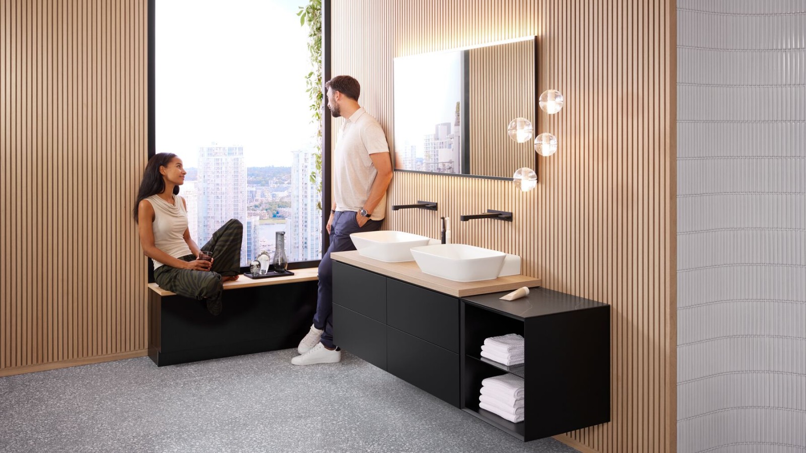 Une femme et un homme dans une grande salle de bains équipée d'un double lavabo Geberit One, d'un miroir Option et d'éléments en bois. Une femme et un homme dans une grande salle de bains équipée d'un double lavabo Geberit One, d'un miroir Option et d'éléments en bois.
