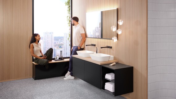 Une femme et un homme dans une grande salle de bains avec des lavabos à poser Geberit ONE, un miroir Option et des éléments en bois. Une femme et un homme dans une grande salle de bains avec des lavabos à poser Geberit ONE, un miroir Option et des éléments en bois.