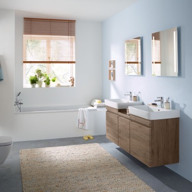 Salle de bains familiale avec mur bleu clair et meubles en noyer hickory, armoire à miroir, plaque de déclenchement et céramiques Geberit