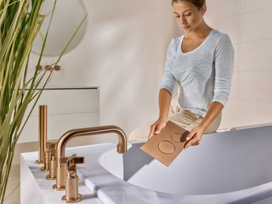 Femme dans la salle de bains avec une plaque de commande Sigma40 en finition cuivre brossé, assortie à la robinetterie Femme dans la salle de bains avec une plaque de commande Sigma40 en finition cuivre brossé, assortie à la robinetterie