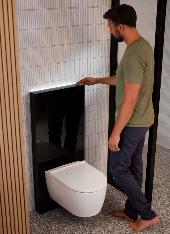 Homme à côté d'un module Geberit Monolith Plus avec ComfortLight Homme à côté d'un module Geberit Monolith Plus avec ComfortLight
